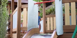 快乐的亚洲小男孩从儿童滑梯上下来。