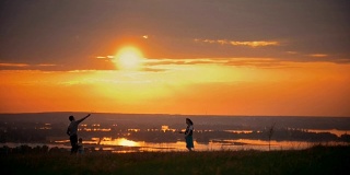 年轻的女子和她的丈夫在球场上打羽毛球，旁边站着他们的小儿子，日落夏夜