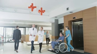 忙碌的医院一楼，医生、护士和工作人员忙碌，接待员与病人交谈，助理移动轮椅上的老人。拥有专业人员的新型现代化医院。视频素材模板下载