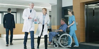 在医院，医生，护士和工作繁忙的人员，接待员与病人谈话，助理移动在轮椅上的老人。拥有专业人员的新型现代化医院。
