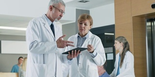 在医院，医生在使用平板电脑时进行讨论。背景:患者与医务人员。新型现代化、功能齐全的医疗设施。