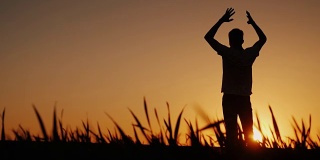 剪影一个年轻人享受新鲜空气，欣赏日落。他把双手放在脑后，看着前方