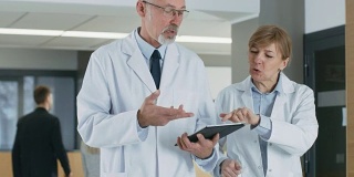 在医院，医生们在大厅边走边用平板电脑讨论。背景:患者与医务人员。新型现代化、功能齐全的医疗设施。