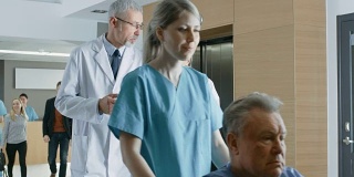 在医院，两位医生走出电梯，一边聊天一边玩平板电脑。背景:患者与医务人员。新型现代化、功能齐全的医疗设施。