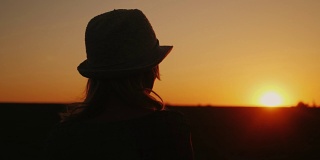 一个戴着帽子的孤独女人看着夕阳。后视图。梦想和规划一个概念