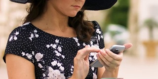 戴帽美女坐在街边咖啡馆，滚动手机应用