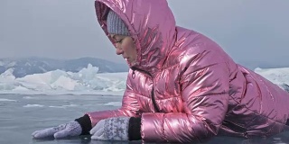 一个女孩走在贝加尔湖破裂的冰面上。一名女旅行者探索并看着一块浮冰。这是自然界中最神奇最纯净的地方。冰环绕着旅行者所有的旅程。