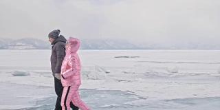 年轻的夫妇有乐趣在冬季散步的背景冰冻结的湖。情侣们走在冰上，手牵着手，亲吻和拥抱。蜜月。爱情故事。