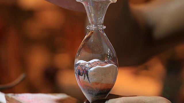 一名男子展示了他的技艺，用彩色沙子制作了一个玻璃花瓶作为纪念品。埃及