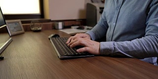 一个穿着蓝色衬衫的男人在键盘上打字。用文档编辑软件编写文档。木制的桌子。机动滑块录像。