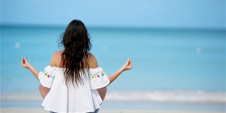 美丽的女孩在热带度假瑜伽姿势。健康的年轻女子坐在瑜伽姿势在海滩上沉思