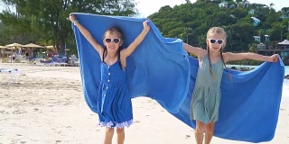 在热带度假期间，小女孩们玩沙滩毛巾玩得很开心