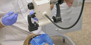 医生使用显微镜。牙医在现代牙科诊所里治疗病人。牙齿矫正师与助手一起工作。作业采用围堰进行。医生和助手戴着防护口罩工作。