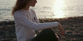 迷人的女孩独自坐在海滩上。