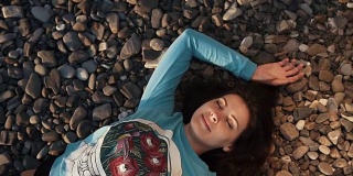 在一个甜蜜的镜头中，漂亮的女人面带微笑躺在岩石海滩上