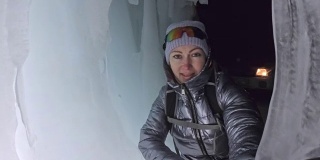 贝加尔湖冰洞上的女游客。观点认为有问题。女孩背包客正在冰洞中行走。游客看着美丽的冰洞。徒步旅行者穿银色夹克，背包，led灯。
