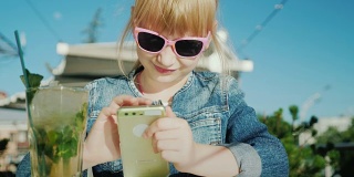 粉色眼镜的有趣女孩在玩智能手机。坐在咖啡馆里的夏日公寓里