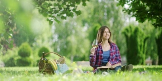 女人在公园野餐时看书和喝白葡萄酒
