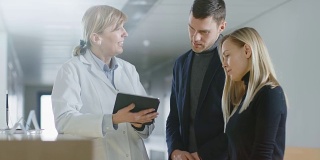 在医院的前台，医生拿着平板电脑与年轻夫妇交谈。