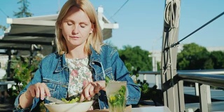 一位年轻女子正在一家餐馆的夏日露台上吃沙拉。在户外吃