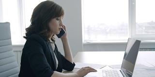 一个成功的女商人，在办公室里一边打电话，一边用笔记本电脑工作