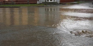雨水落在路上，流过下水道。汽车在被水淹没的道路上行驶。
