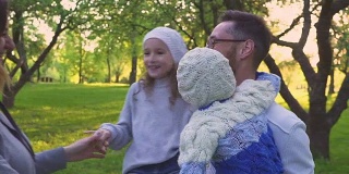 幸福的一家人在草地上拥抱。父母和他们的两个女儿在公园的草坪上拥抱。花期果园。