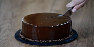 给巧克力慕斯蛋糕上釉，特写。用刀切一块巧克力蛋糕