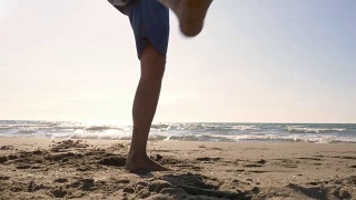 一个年轻人穿着泳裤在海滩上表演花样，用脚拿着足球在海滩上的日落剪影视频素材模板下载