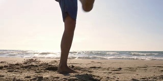 一个年轻人穿着泳裤在海滩上表演花样，用脚拿着足球在海滩上的日落剪影