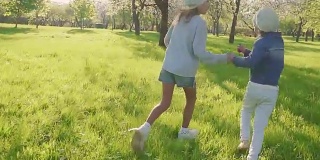 孩子们在开满鲜花的果园的公园里奔跑。斯坦尼康拍摄的两个女孩跑过公园和微笑。慢动作