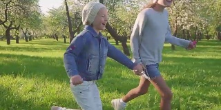 孩子们在开满鲜花的果园的公园里奔跑。斯坦尼康拍摄的两个女孩跑过公园和微笑。慢动作