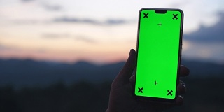 男人拿着智能手机的绿色屏幕与自然戏剧性的天空为背景，色度键