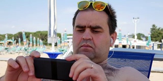 暑假，科技和人的概念-快乐的年轻人戴着太阳镜与智能手机和耳机听音乐和沙滩浴巾日光浴