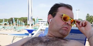 暑假，科技和人的概念-快乐的年轻人戴着太阳镜与智能手机和耳机听音乐和沙滩浴巾日光浴