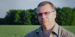 一个戴着眼镜的中年农民的肖像，背景是一片绿色的田野
