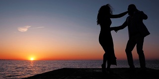 年轻的西班牙夫妇的剪影在夕阳下的大海背景。男人和女人跳舞拉丁美洲的感官舞蹈:bachata, salsa或kizomba。慢动作