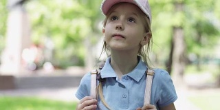 一个可爱的金发小女孩戴着帽子，穿着短裤在公园里散步。