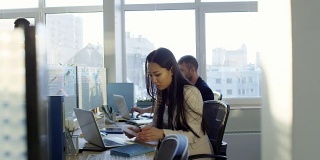 年轻的亚洲女士与同事在开放空间办公室工作