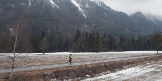 冬季，在积雪覆盖的山顶下，一名飞行员在一条穿越山谷的小道上奔跑