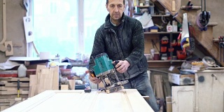 这位65岁的老师傅正在用电动手铣床工作。木工上的小家具厂。