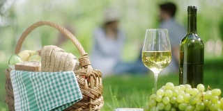 公园里的白葡萄和一瓶白葡萄酒，背景是一对浪漫的情侣