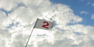在晴朗多风的日子，明亮的多云背景上的高尔夫旗帜。