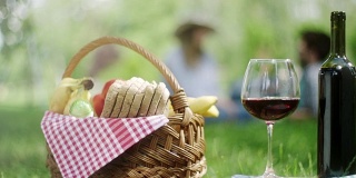 公园里的红葡萄和一瓶红酒，背景是一对浪漫的情侣