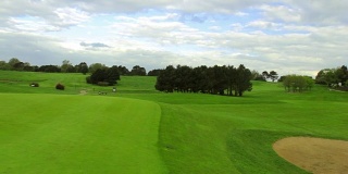 在一个晴朗多风的日子里，一个绿色的高尔夫球场，洞和旗子。