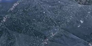 雪在冰面上飞舞。雪花在贝加尔湖的冰面上飞舞。冰非常美丽，有独特的裂缝。雪花闪耀着红光。在日落时分。高对比度。