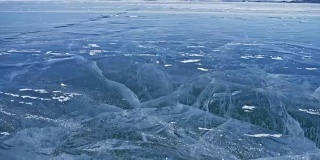 雪在冰面上飞舞。雪花在贝加尔湖的冰面上飞舞。冰非常美丽，有独特的裂缝。背景视图山景。雪花闪耀着红光。