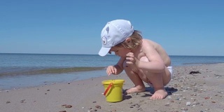 金发小男孩在海边玩耍。孩子在海边的沙滩上走着，玩着沙子和玩具。