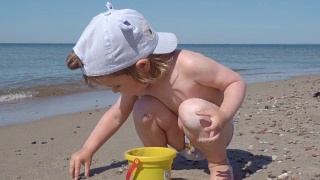 金发小男孩在海边玩耍。孩子在海边的沙滩上走着，玩着沙子和玩具。视频素材模板下载