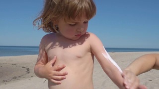 妈妈在海滩上给儿子涂防晒霜。母亲为孩子准备在海里洗澡。视频素材模板下载